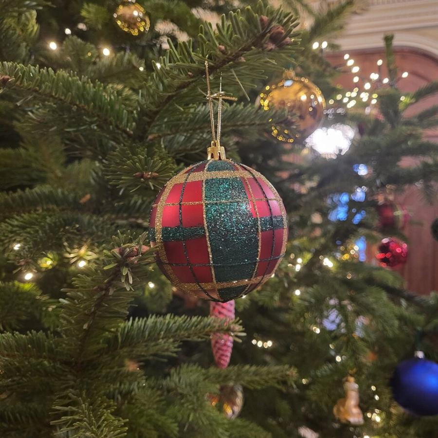 Fragment udekorowanej choinki. W centrum kadru zielono-czerwona bombka.